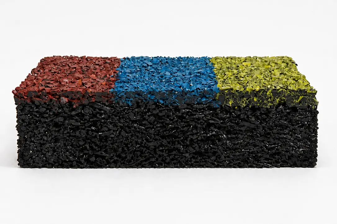 Corte de uma amostra do piso: base preta de borracha reciclada e camada superior pigmentada em vermelho, azul e verde