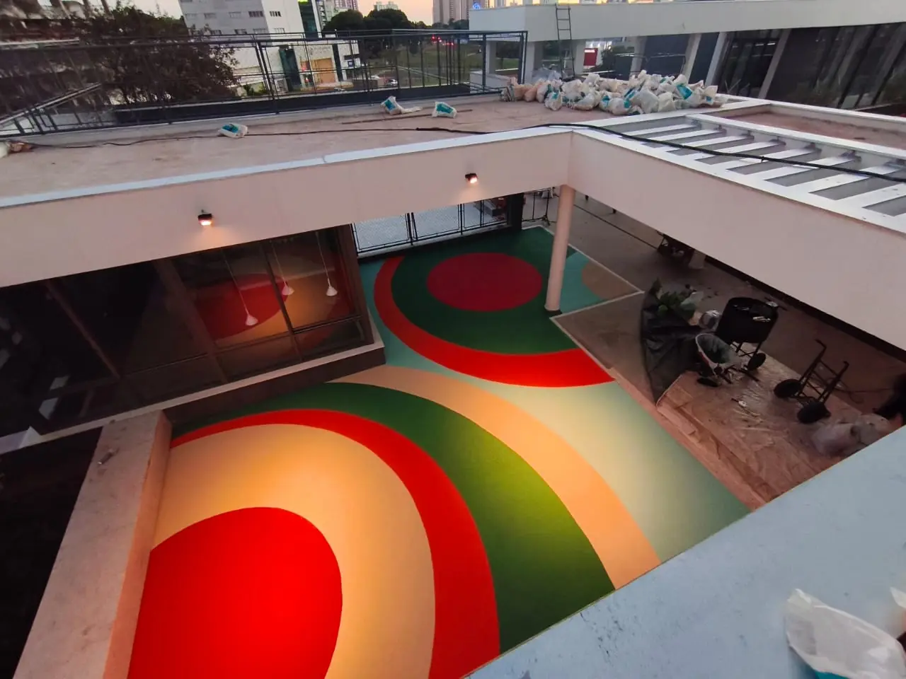 Área de convivência com piso monolítico EPDM em círculos concêntricos vermelho, laranja e verde na obra da Plaenge, Campo Grande/MS