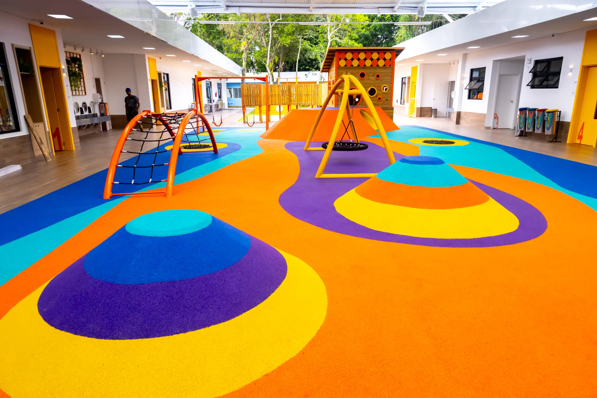 Piso monolítico EPDM laranja, roxo e turquesa com morrotes e brinquedos no Colégio Positivo Vila Olímpia, Florianópolis/SC