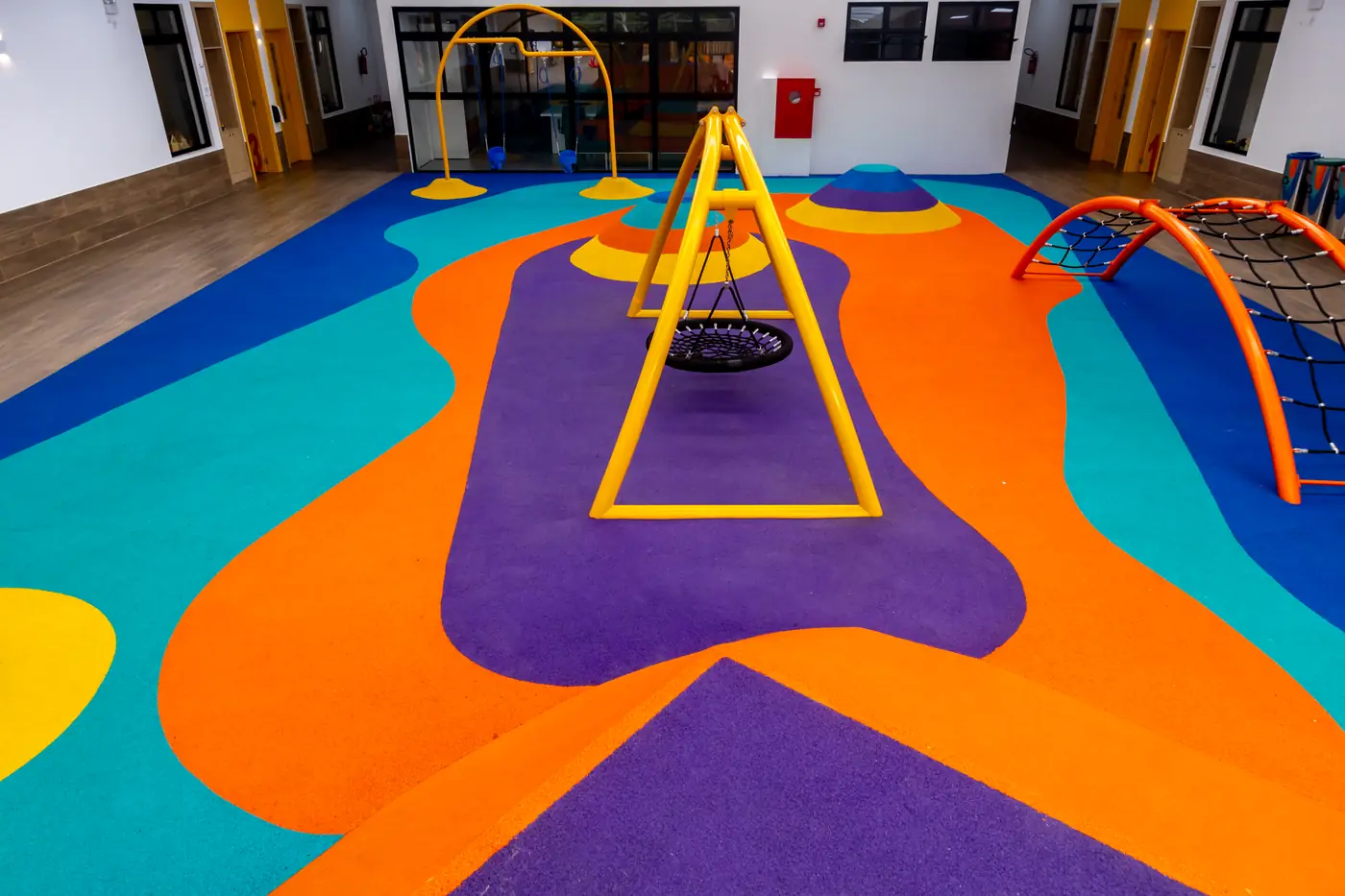 Balanço amarelo sobre piso monolítico EPDM laranja, roxo e azul no Colégio Positivo Vila Olímpia, Florianópolis/SC