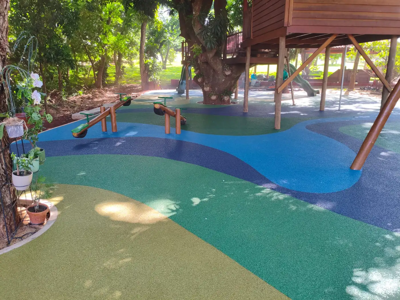 Playground de madeira sob as árvores com piso monolítico SBR azul e verde na Fazenda Tília, Rolândia/PR
